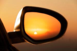 Blick auf den Sonnenuntergang durch den Rückspiegel eines Autos.