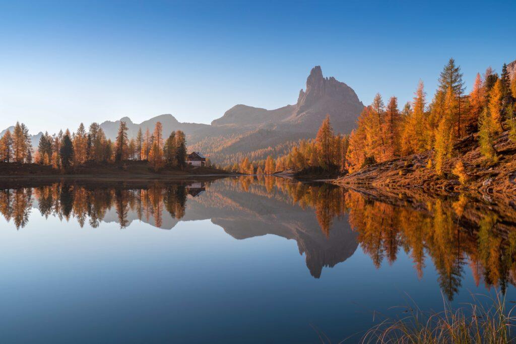 Herbstlicher Blick auf den Federasee in den Dolomiten bei Sonnenuntergang. Fantastische Herbstszene mit blauem Himmel, majestätischem Felsberg und bunten Bäumen, die im Sonnenlicht in den Dolomiten glänzen.