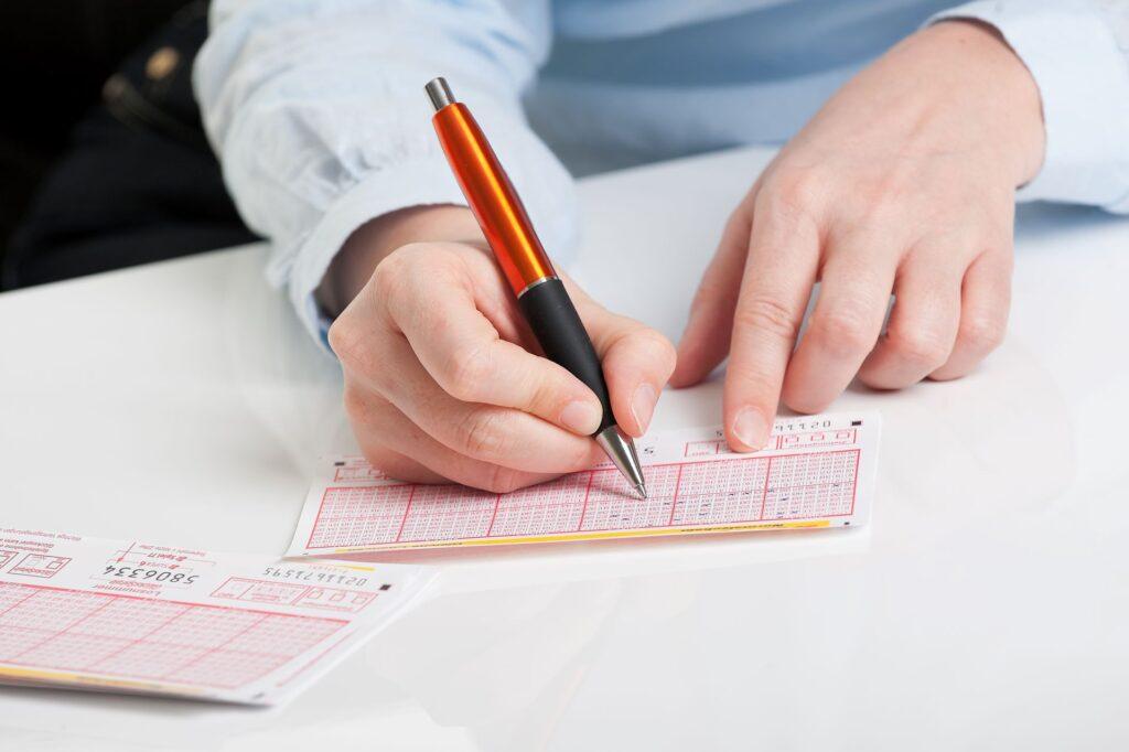 Nahaufnahme einer Hand, die mit einem Stift einen Lottoschein ausfüllt, unter Anwendung eines Lottozahlen Vorhersage Tricks.