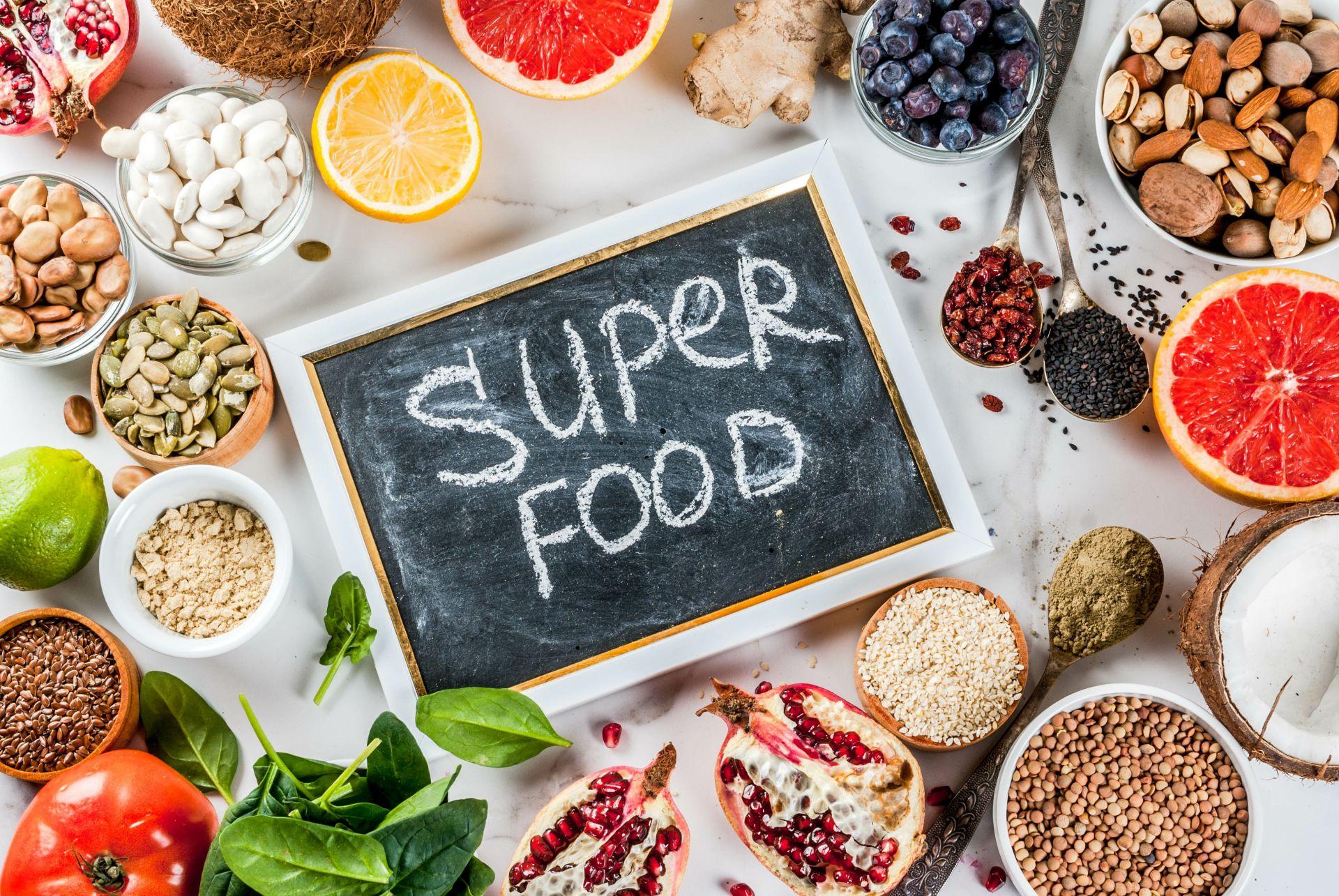 Auswahl an Superfoods wie Granatapfel, Samen, Beeren und Gemüse mit einer Kreidetafel, die "Superfood" anzeigt. Ideale Visualisierung für die Vorteile von Bio Lebensmitteln.