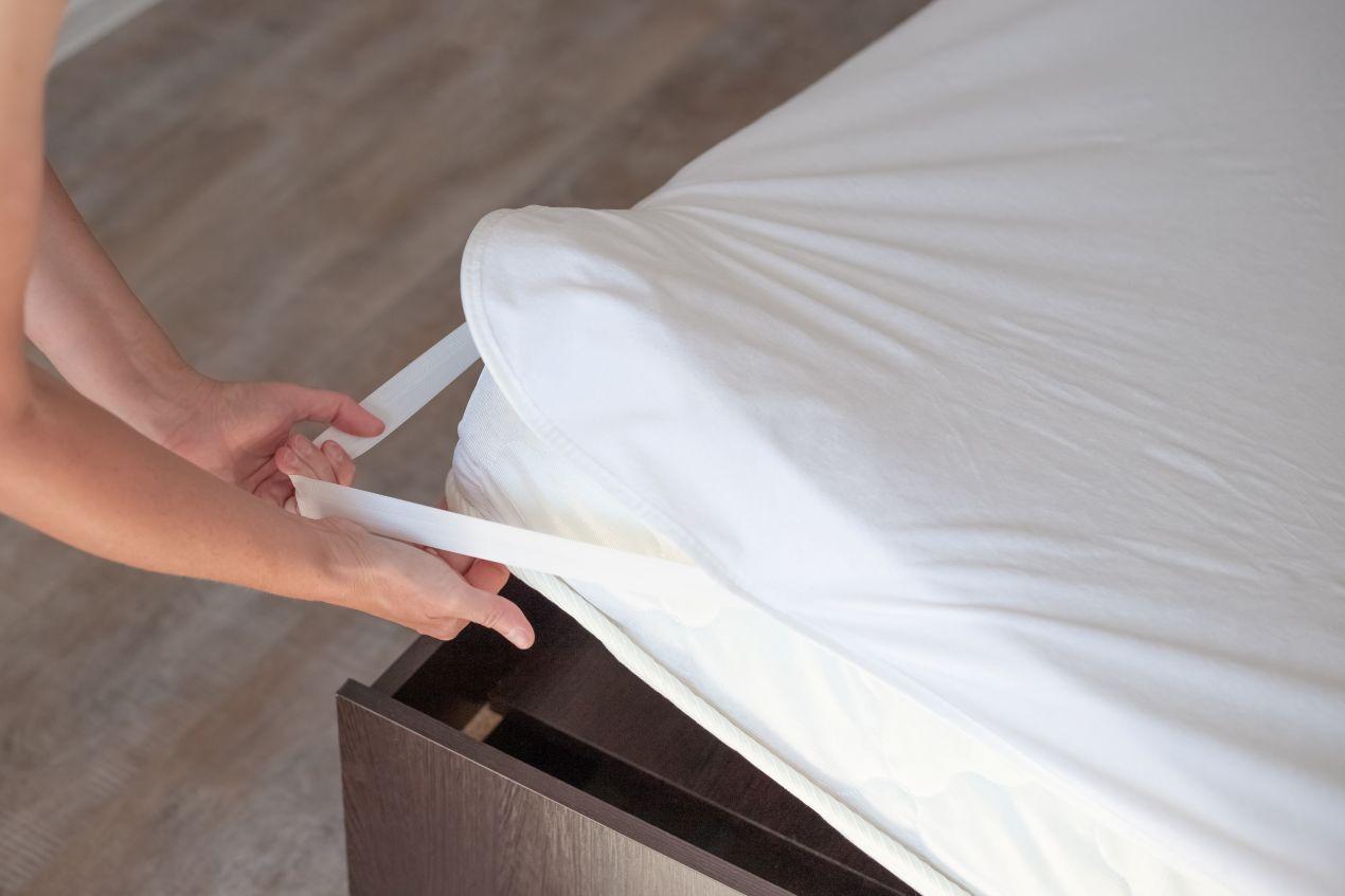 Nahaufnahme vom Aufziehen eines Matratzenschutzes mit elastischen Baendern auf eine Matratze in einem modernen Bettgestell