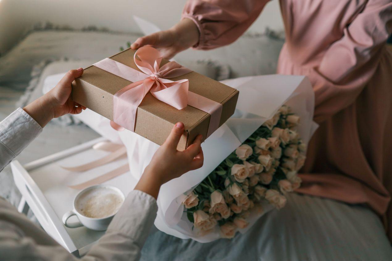 Geschenk mit rosa Schleife wird als geburtstagsgeschenk zusammen mit Blumen ueberreicht