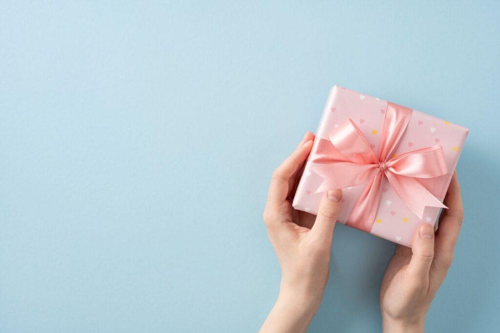 Rosa geburtstagsgeschenk mit Schleife in Haenden vor hellblauem Hintergrund