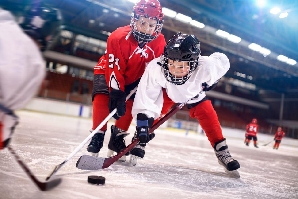 Zwei Kinder im Eishockey-Zweikampf kaempfen um einen Eishockey Puck auf einer Eisbahn mit Flutlicht