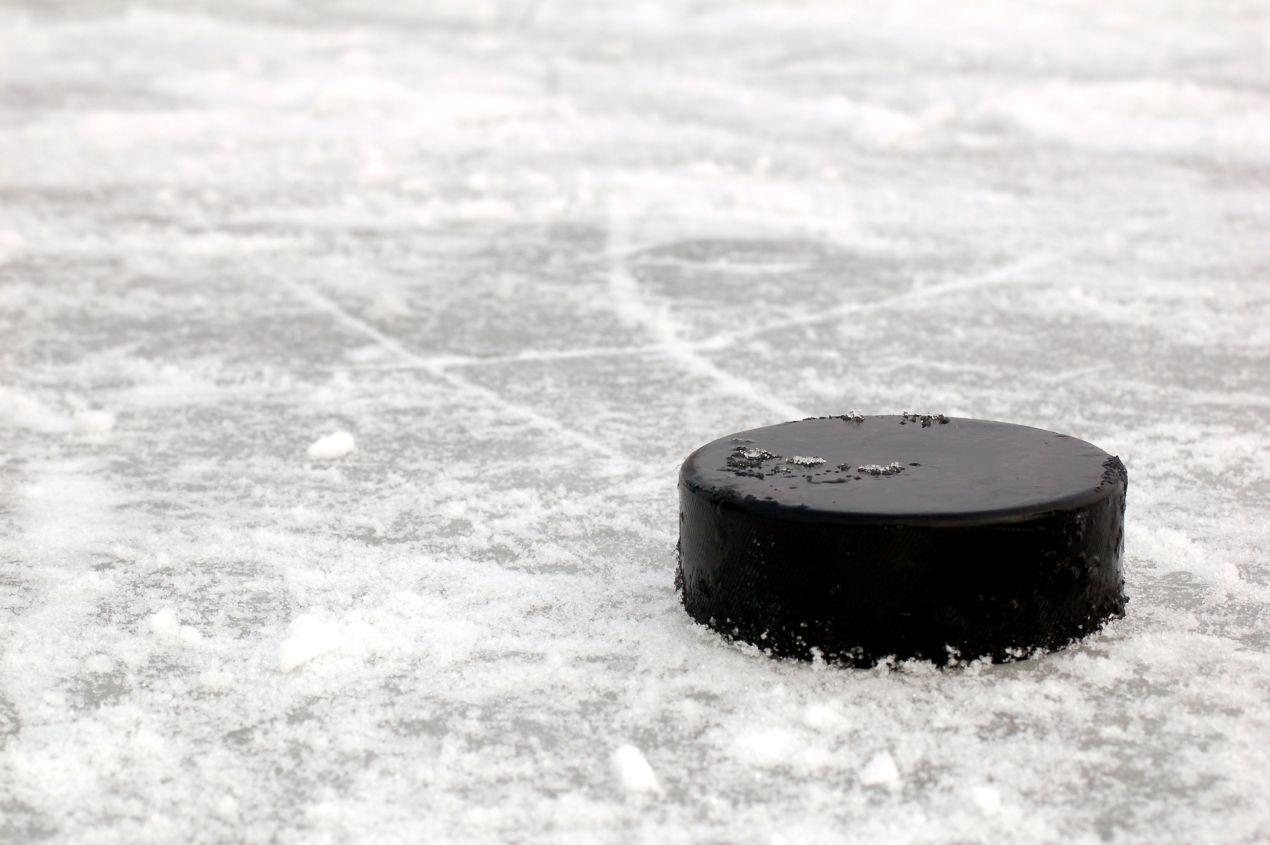 Ein einzelner Eishockey Puck liegt auf rauem Eis mit Eissplittern und Spuren vom Spielbetrieb